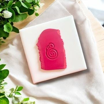 Twisted flamingo clay imprint on pink polymer clay, displayed on a white tile with fresh greenery accents.
