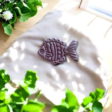 Finished purple polymer clay fish charm with detailed scales and fins, styled beautifully with greenery on soft fabric.