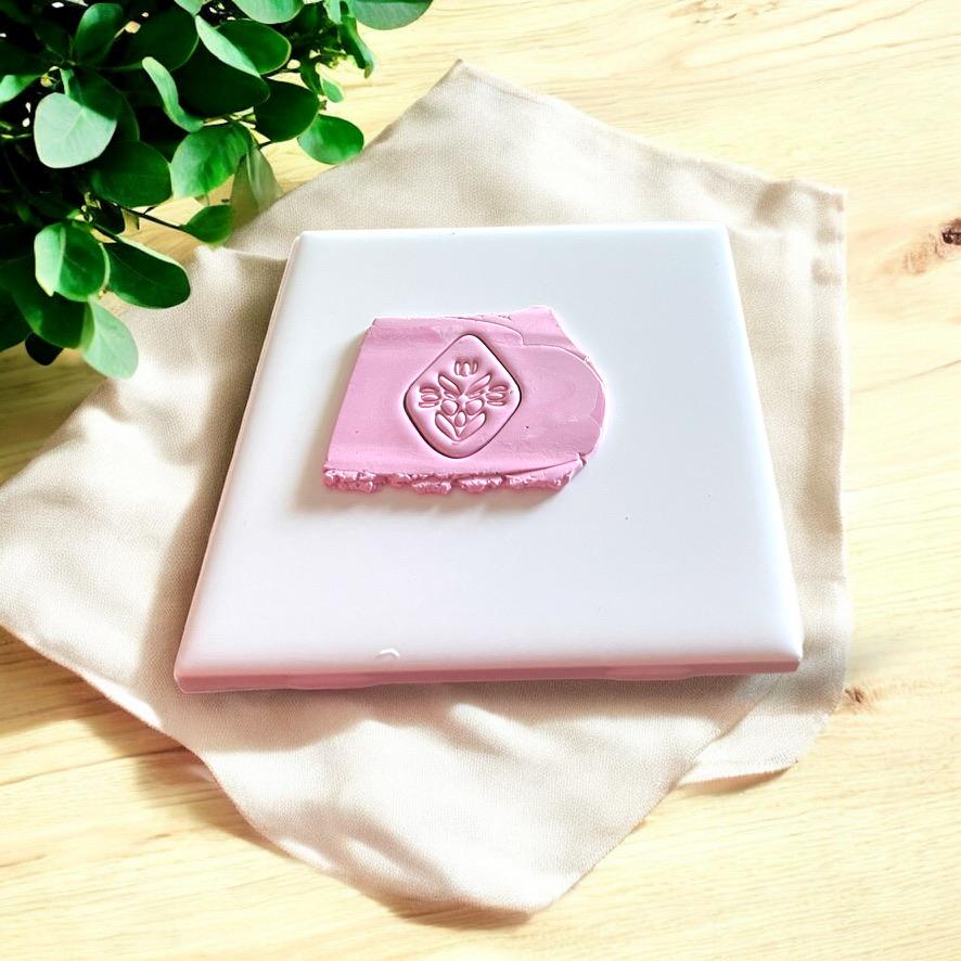 Polymer clay cut shape of a folk art inspired flower on a white tile surrounded by soft neutral fabric