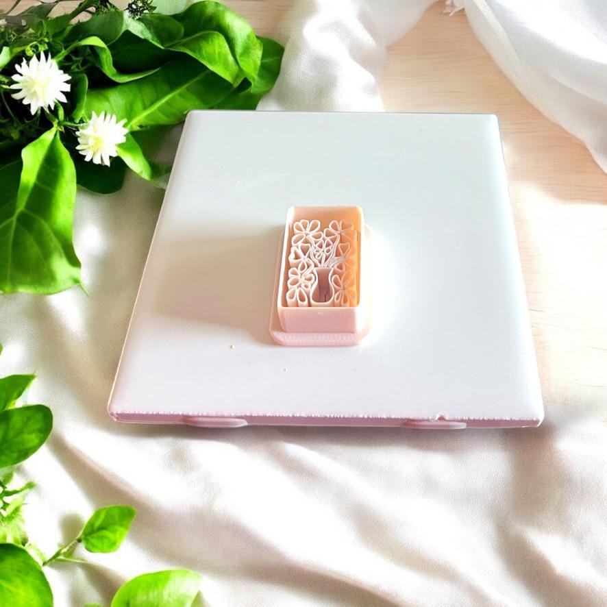 Flower vase clay cutter beside matching floral clay impression on white tile.