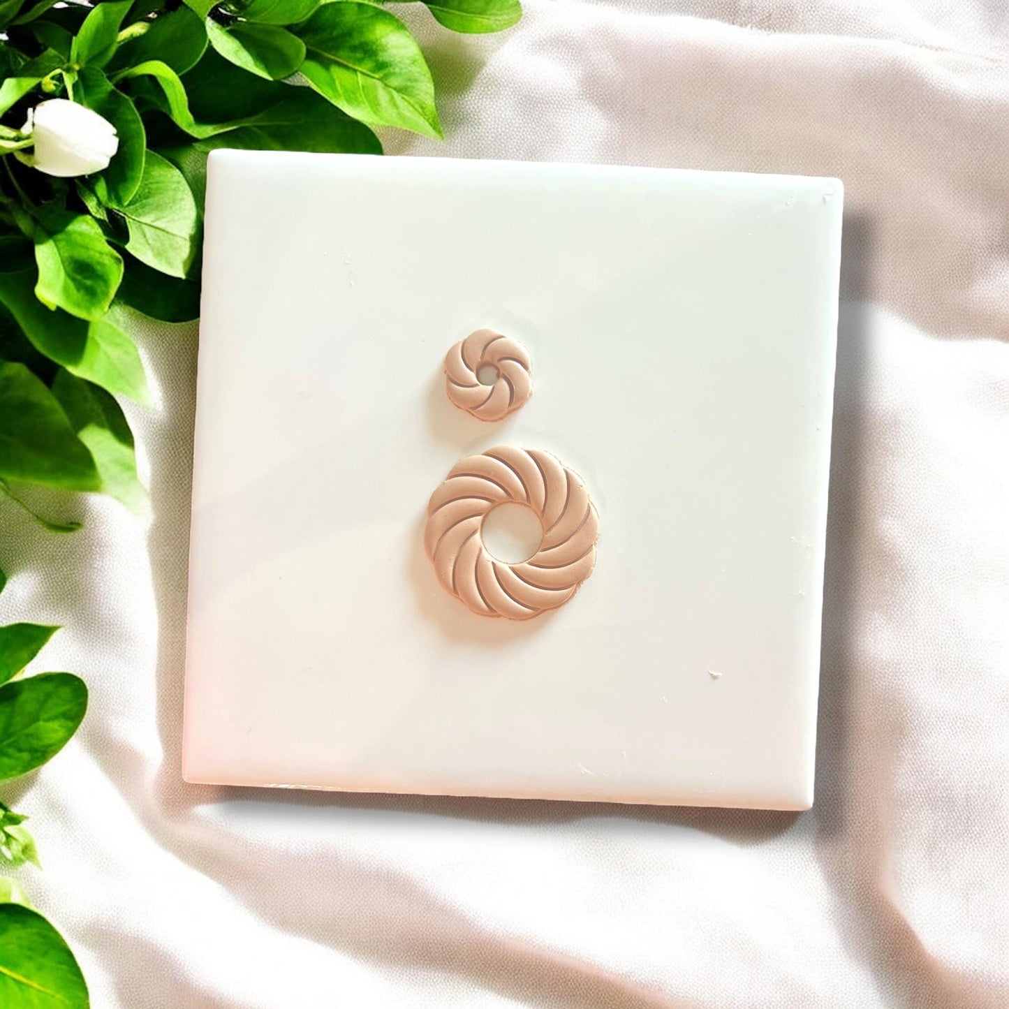Finished swirl shell polymer clay charms displayed on white tile with greenery.