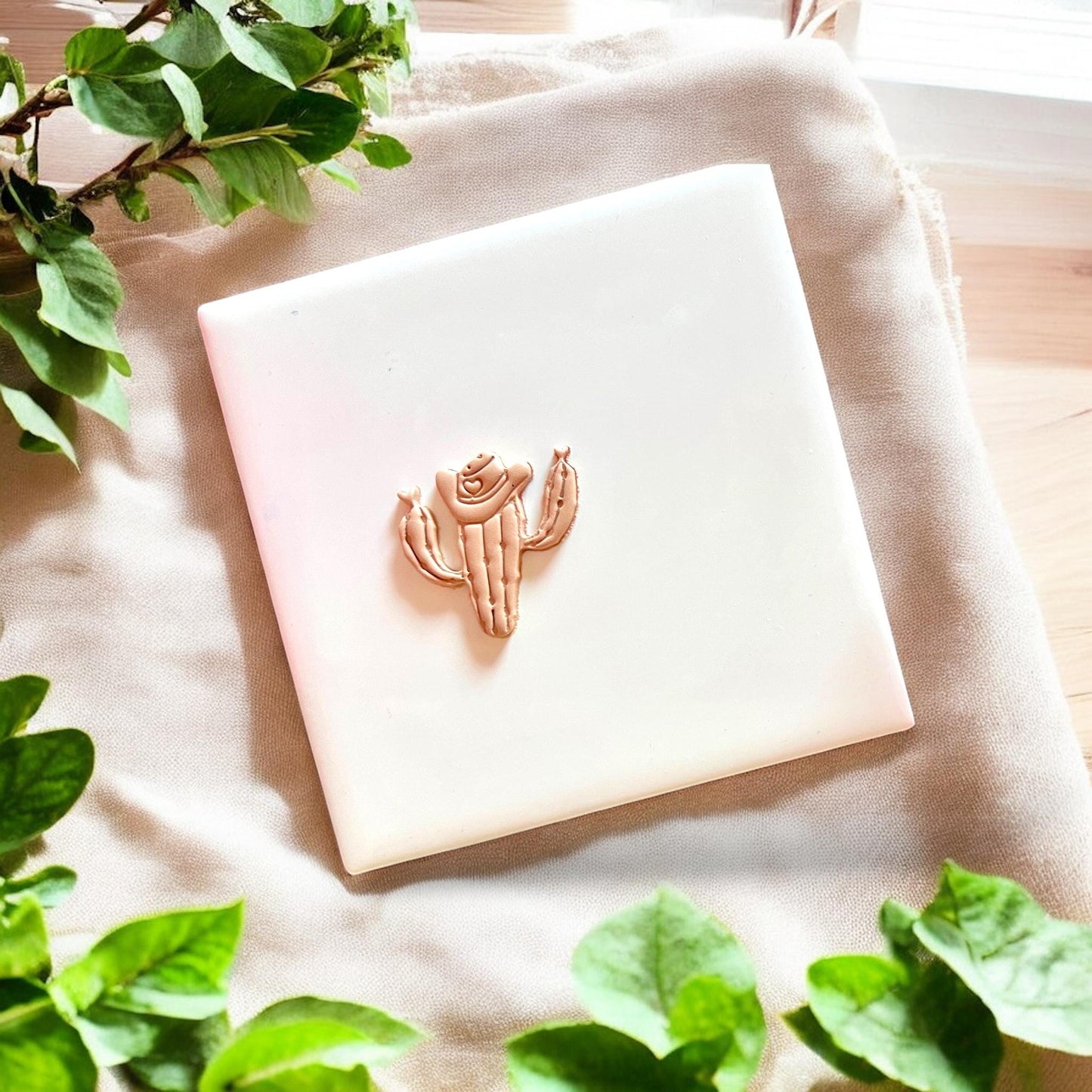 A finished cowboy cactus shape in tan clay displayed on a white tile.