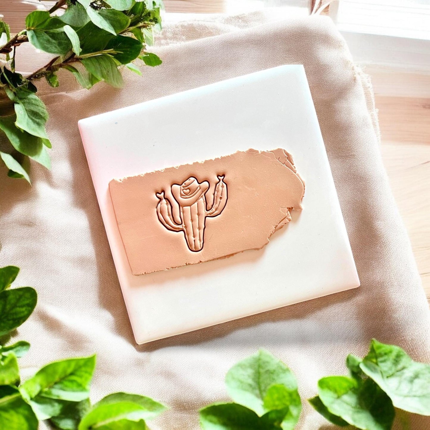 A tan slab of polymer clay pressed with a cowboy cactus cutter showing crisp line detail.