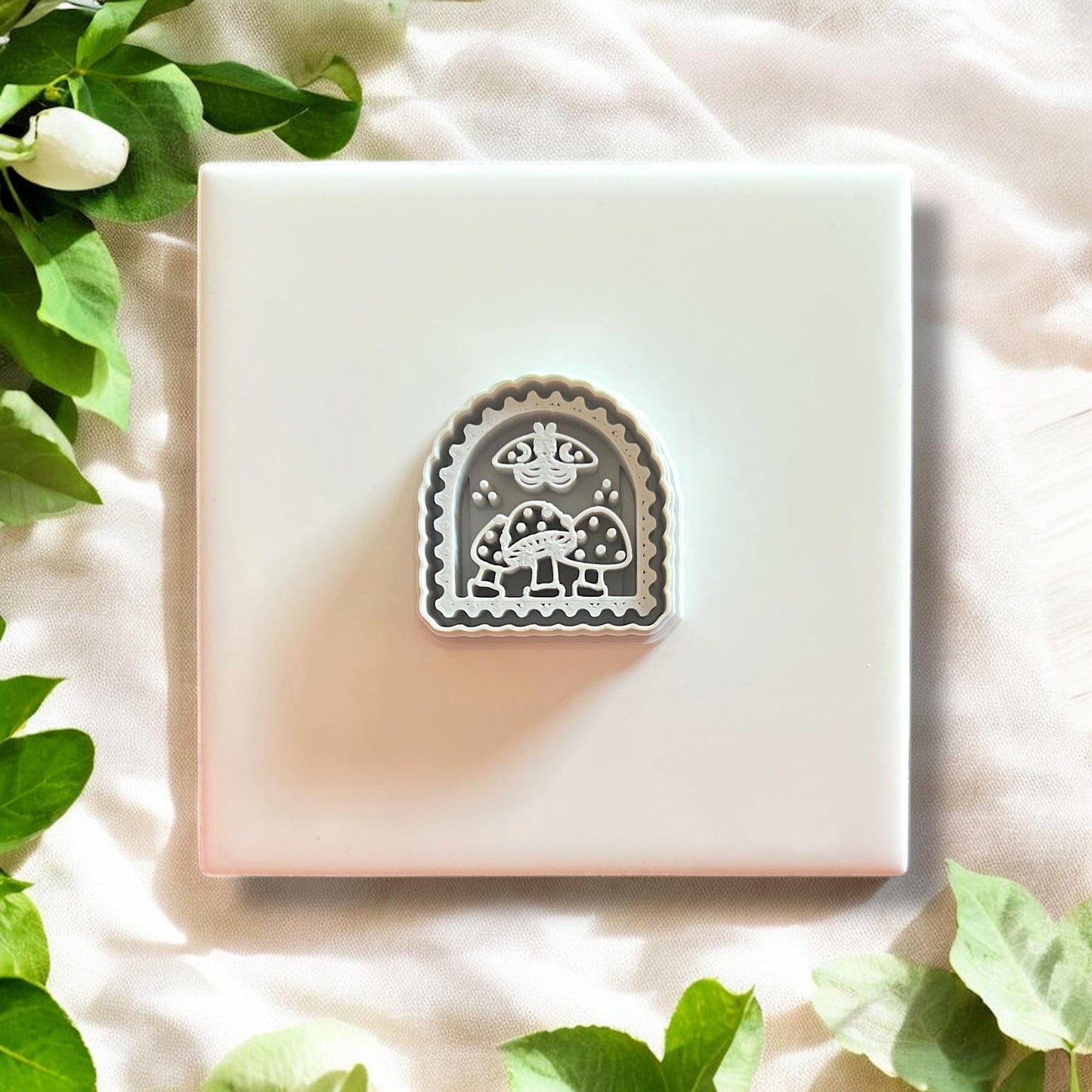 Gray boho moth and mushroom arch clay cutter displayed solo on a white tile with greenery.