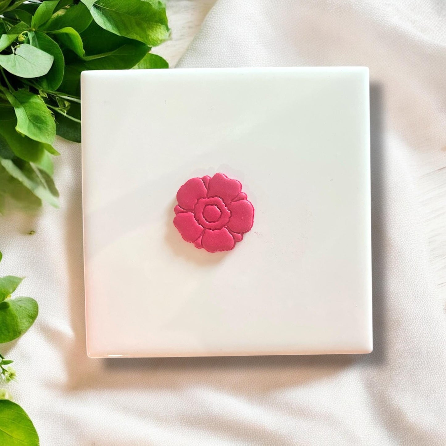 Finished pink clay cutout shaped like an anemone flower displayed on white tile