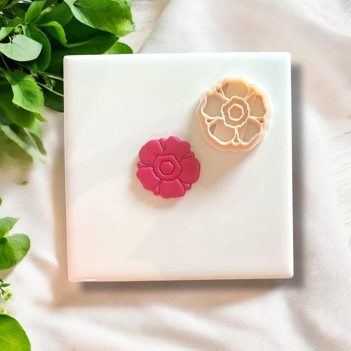 Side-by-side view of pink floral clay piece and coordinating flower-shaped cutter