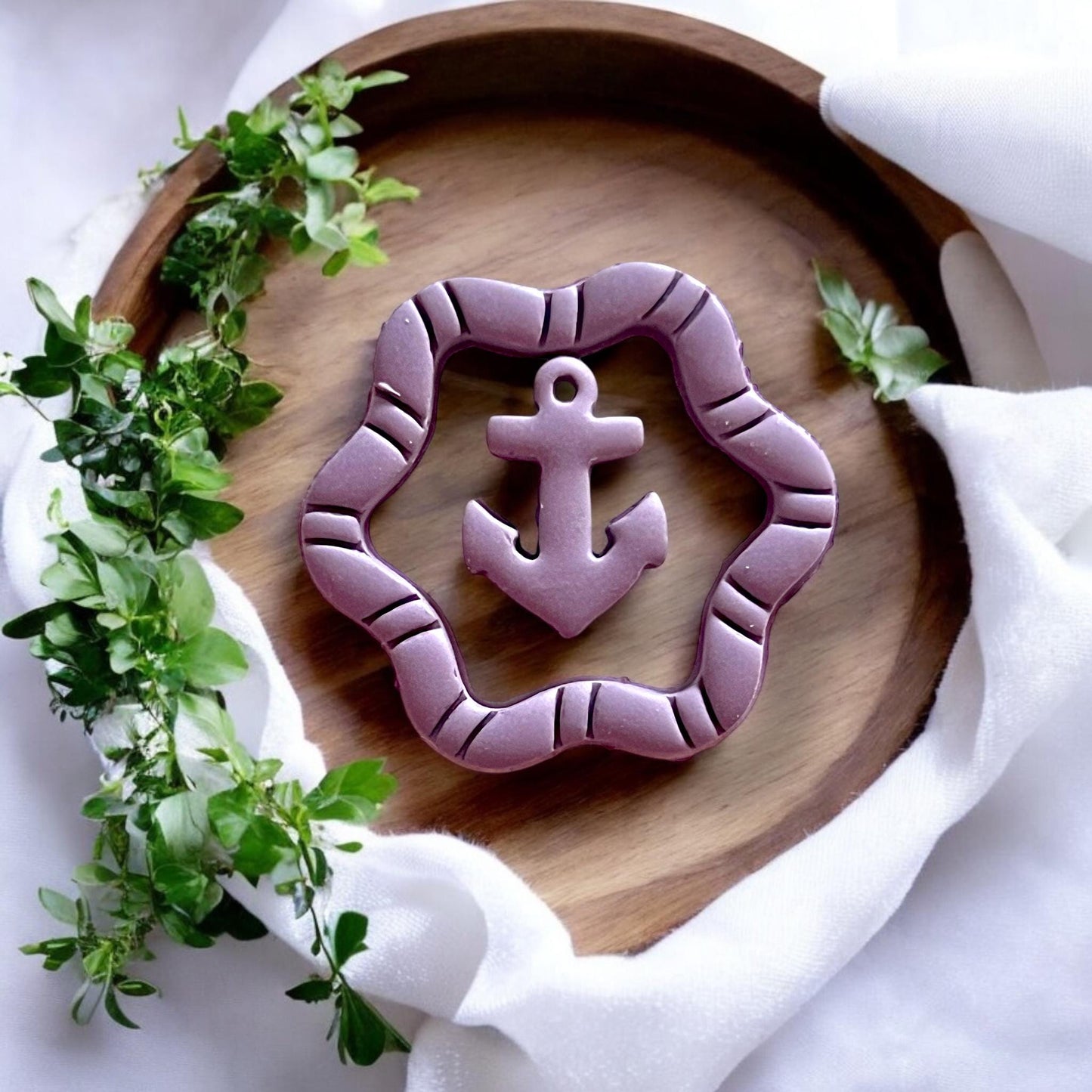 Finished clay anchor earring piece inside rope frame on wood tray