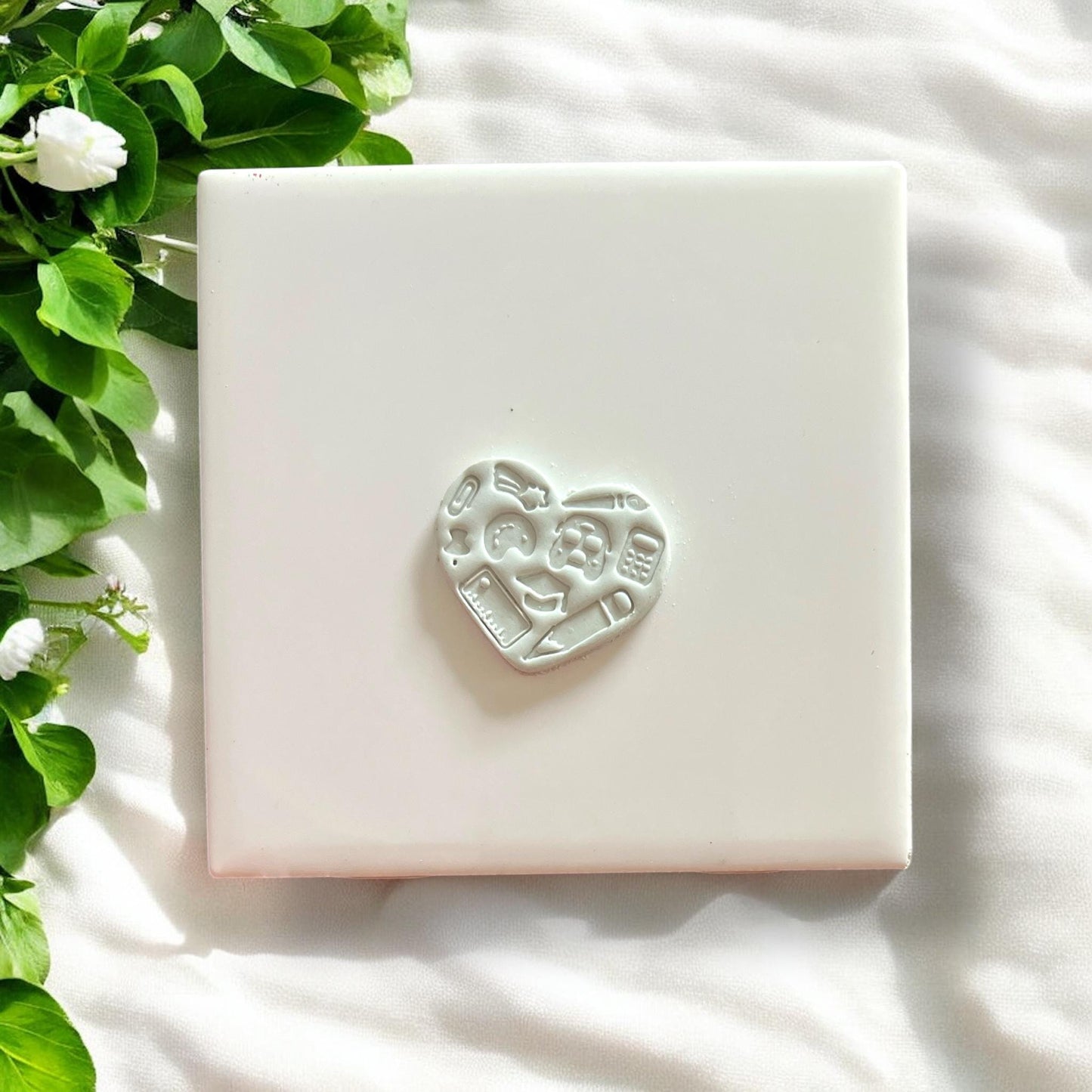 White heart cut from clay showing embossed classroom tools like ruler, apple, and pencil