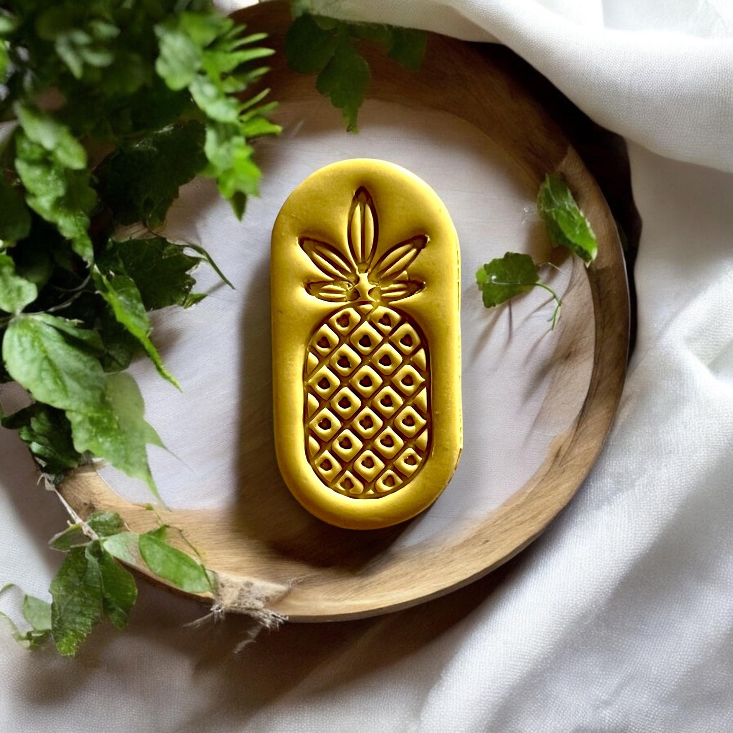 Finished pineapple clay dangle displayed on wood plate with greenery