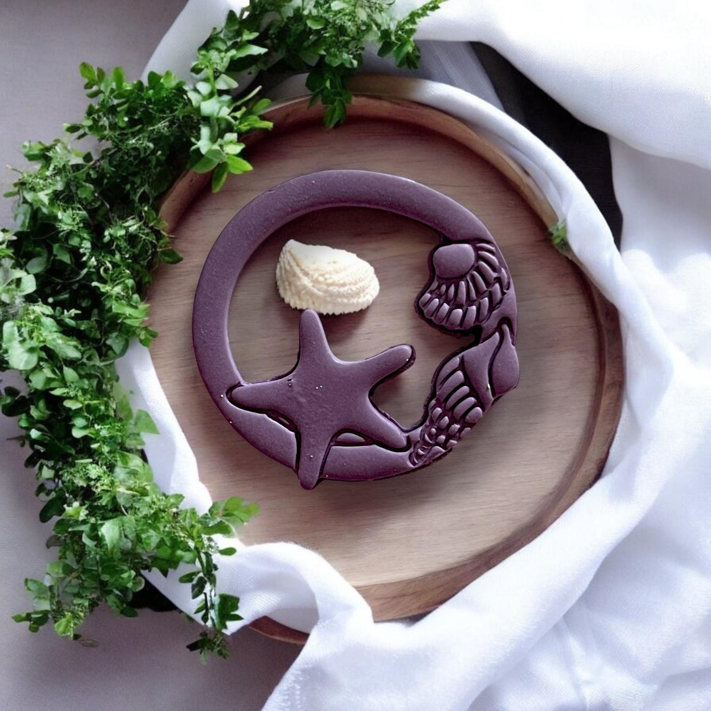 Finished clay piece styled on wood with soft fabric and seashell, highlighting coastal detail from the cutter