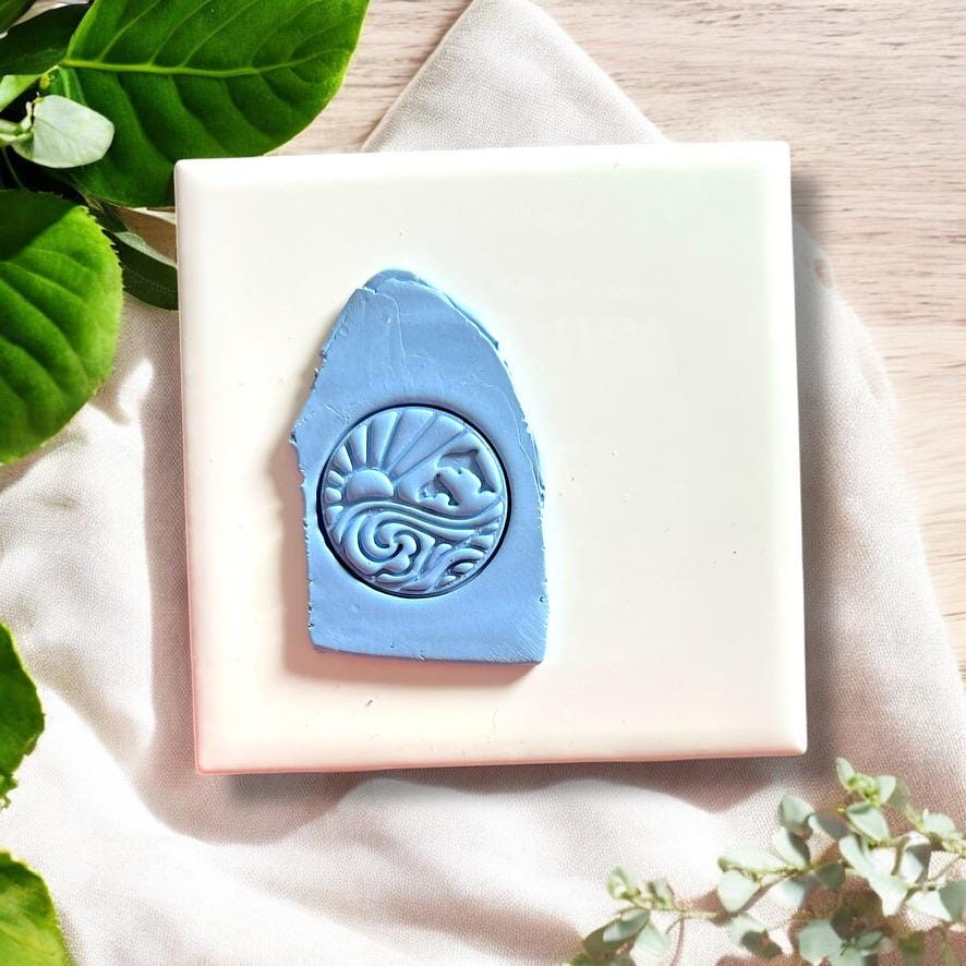 Round polymer clay stamp showing dolphin, sun, and sea perfect for earrings