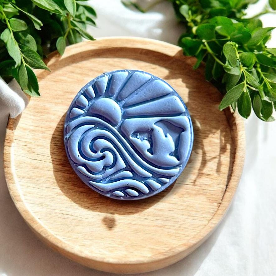 Finished dolphin and wave earring in blue clay shown on wooden tray