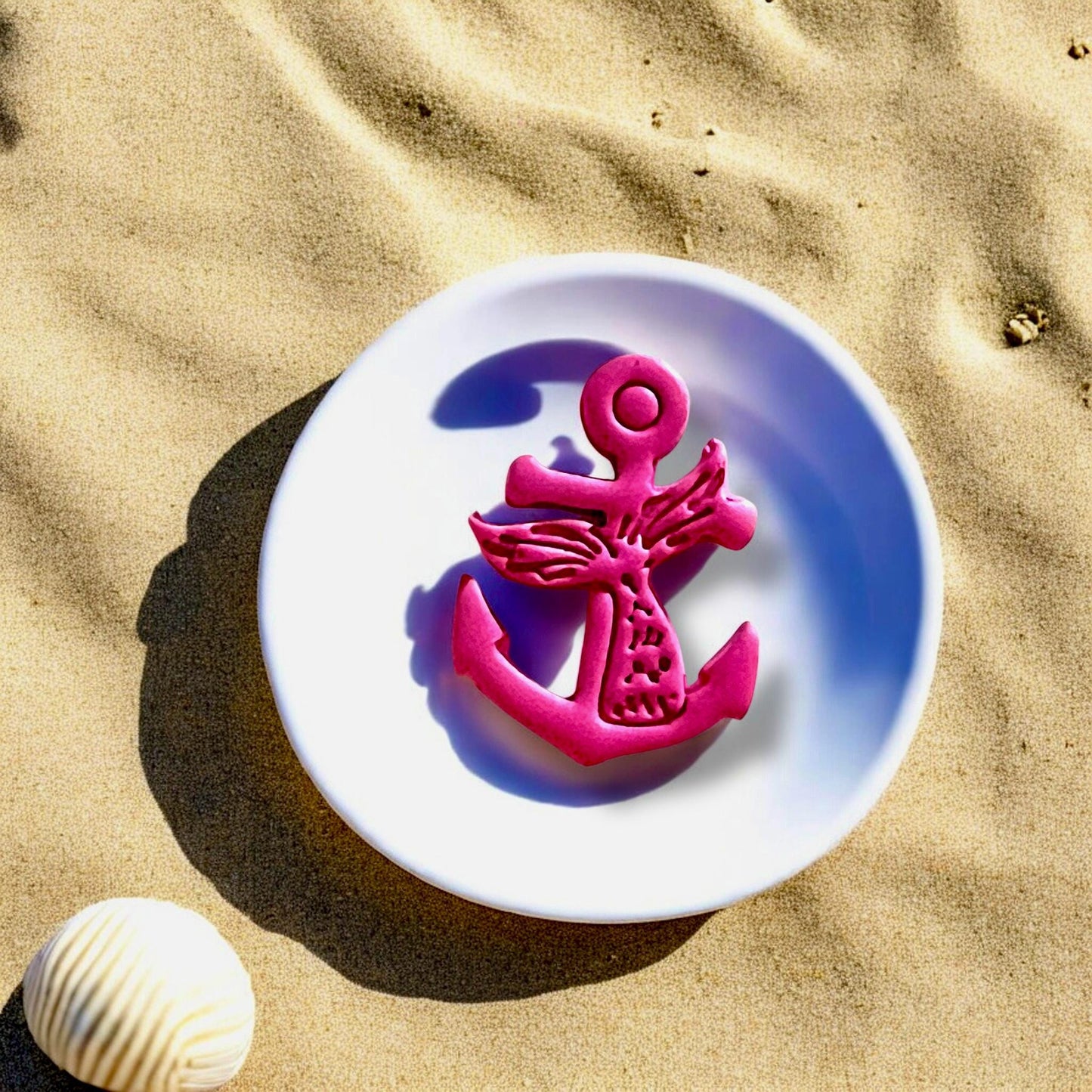 Mermaid tail anchor cutter impression in large pink polymer clay, displayed on a white dish with beach sand and seashell.