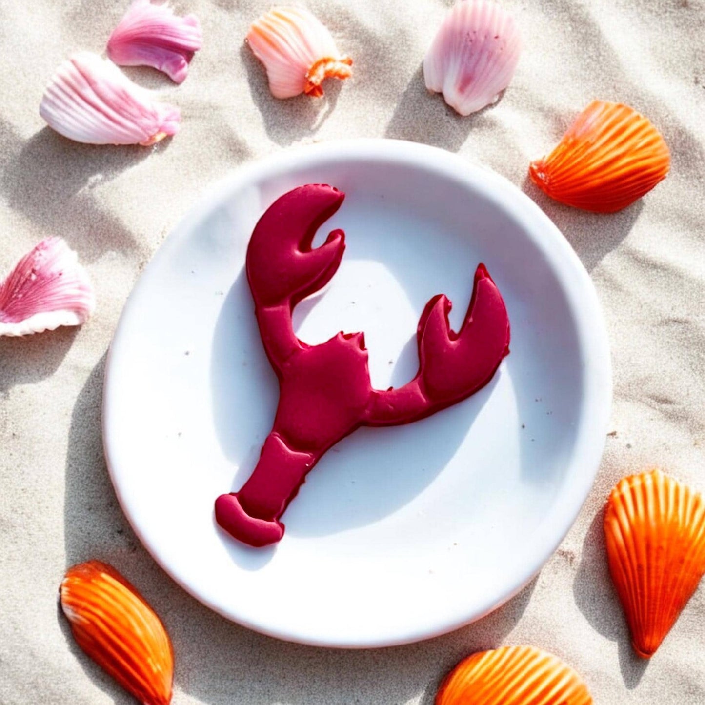 Bright pink lobster clay cutout surrounded by orange and pink seashells