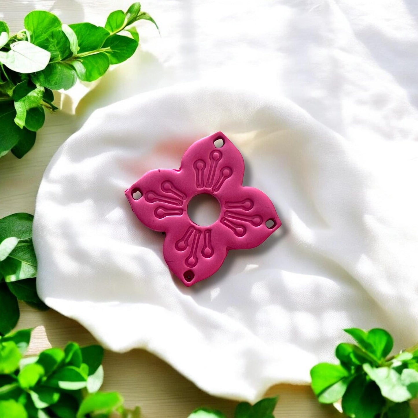 Close-up of finished floral clay piece with four petals and drilled corner holes