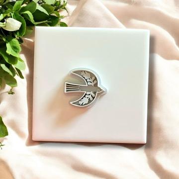 Gray folk bird clay cutter in a Scandinavian style, displayed on a white tile with soft fabric and fresh green leaves.