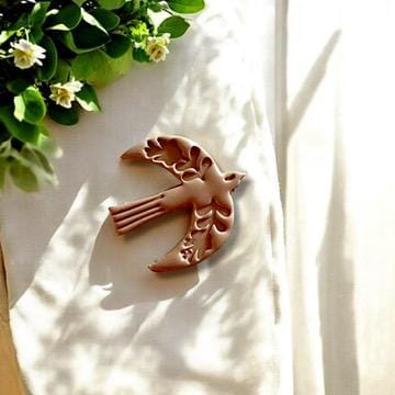 Large polymer clay bird charm in Scandinavian folklore style, displayed beautifully with greenery on soft fabric.