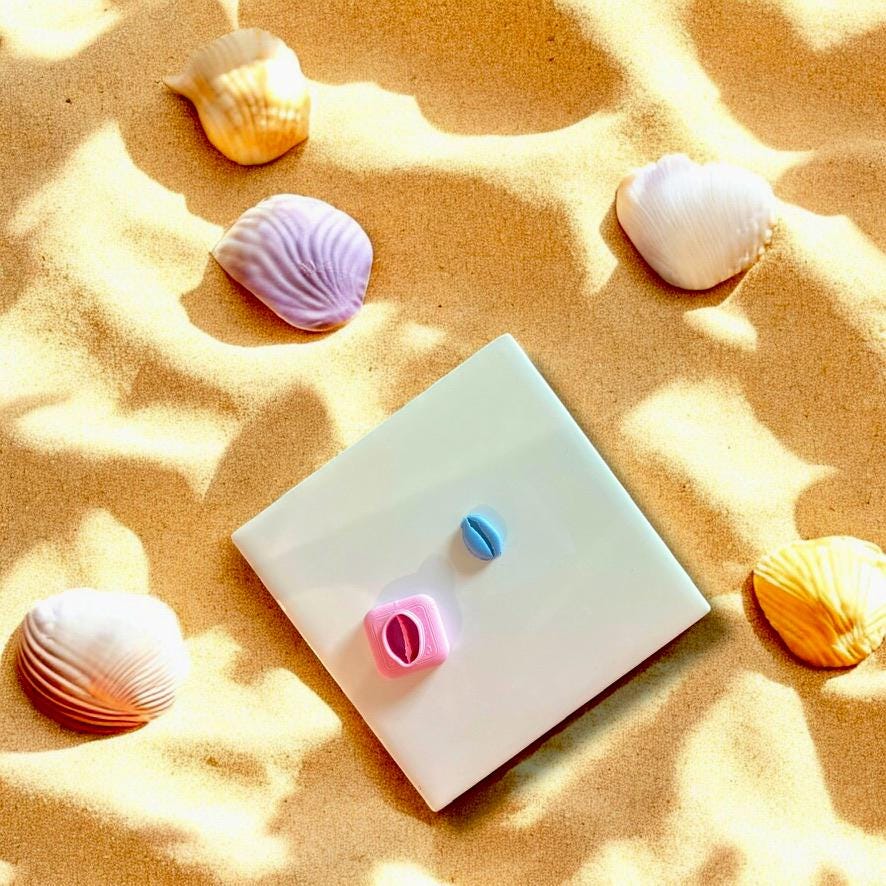 Polymer clay cowrie shell charm with its matching cutter, displayed on beach sand with pastel-colored seashells.