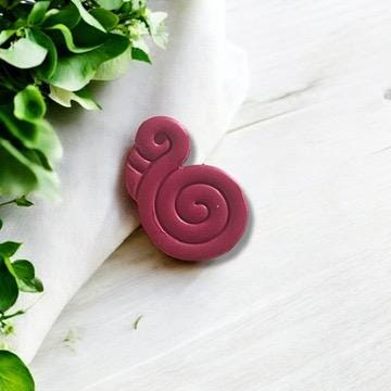 Pink polymer clay flamingo charm with a twisted style, displayed beautifully with soft greenery for a summer vibe.