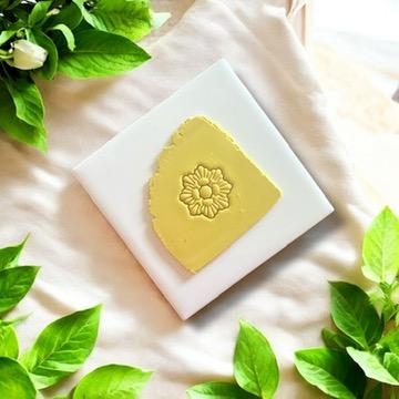 Seashell wreath clay imprint on yellow polymer clay, displayed on a white tile with fresh greenery accents.