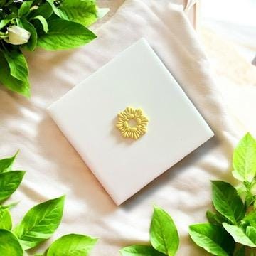 Yellow polymer clay seashell wreath charm displayed on a white ceramic tile, perfect for beach-themed jewelry.