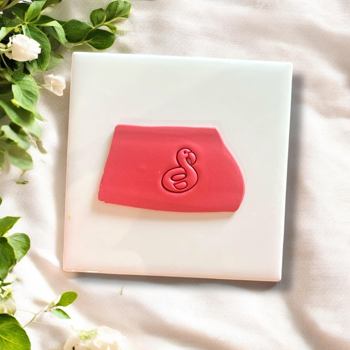 Pink polymer clay impression of flamingo floatie design on white tile with greenery in the background.