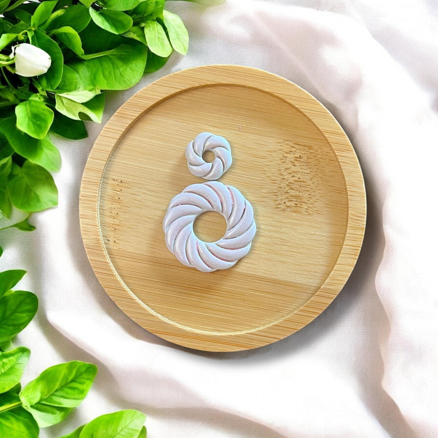Finished swirl shell earrings on a bamboo tray, with green leaves and white fabric background.