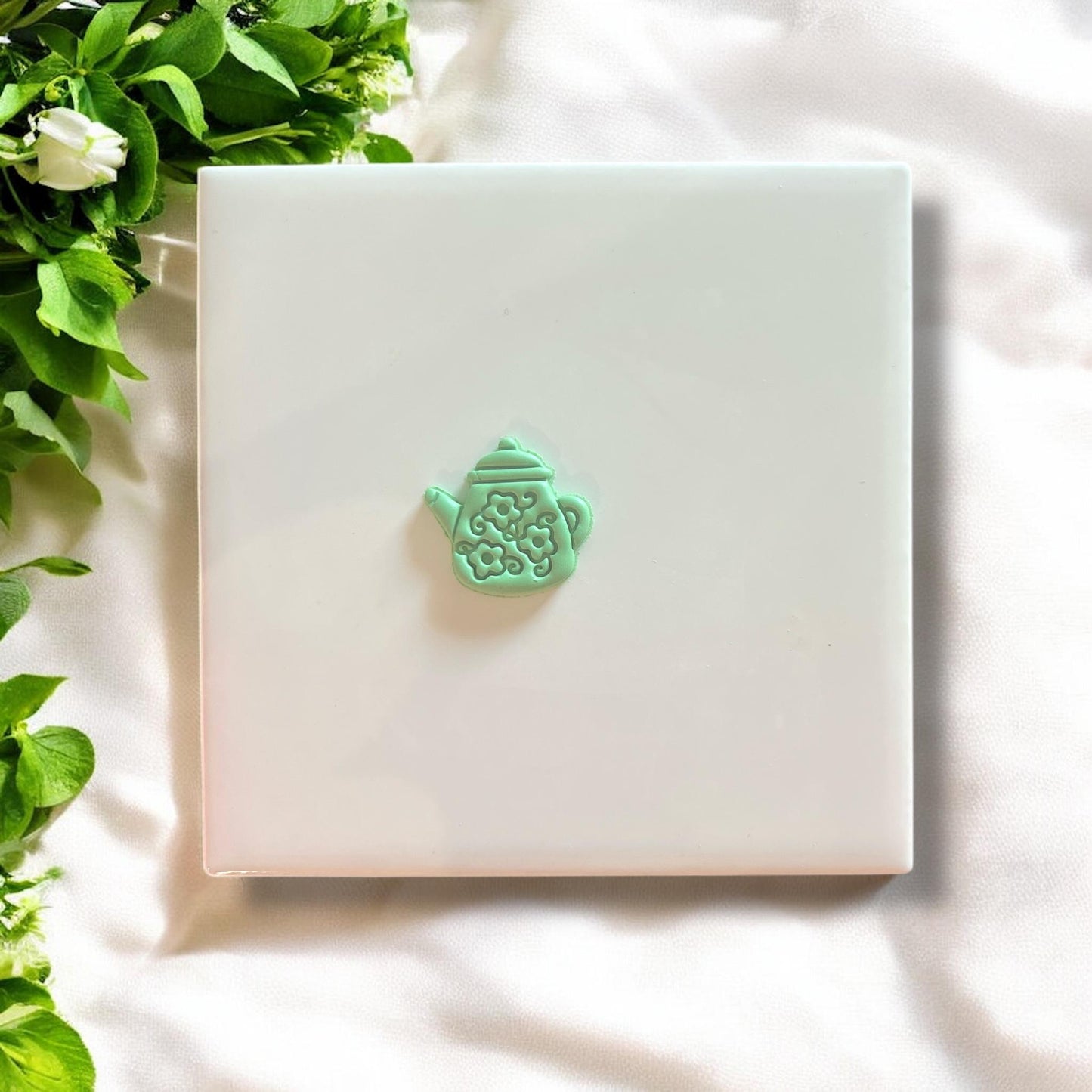 Finished floral teapot charm in green polymer clay, displayed on a white tile.