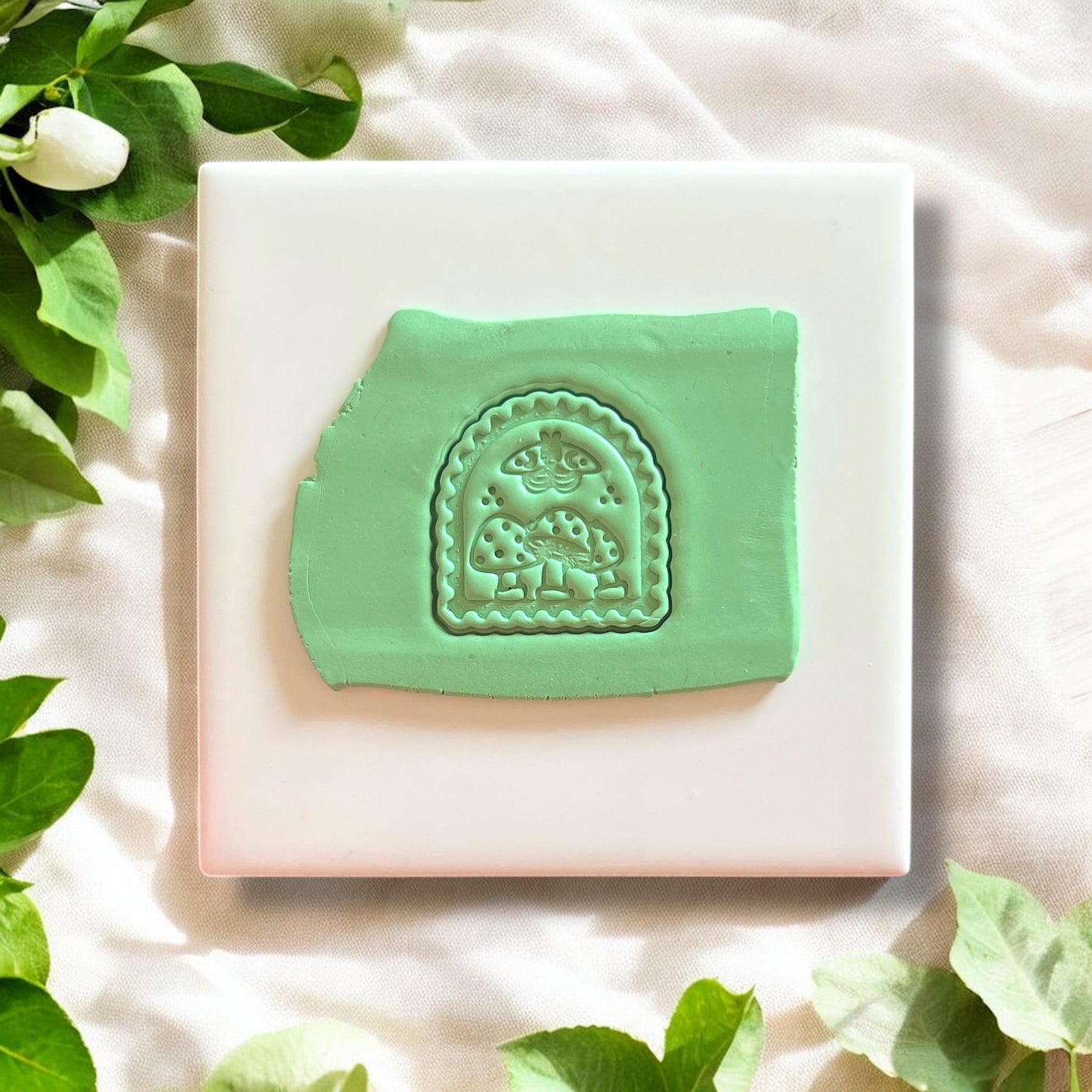 Fresh clay impression of mushroom moth arch design in green clay on a white ceramic tile.
