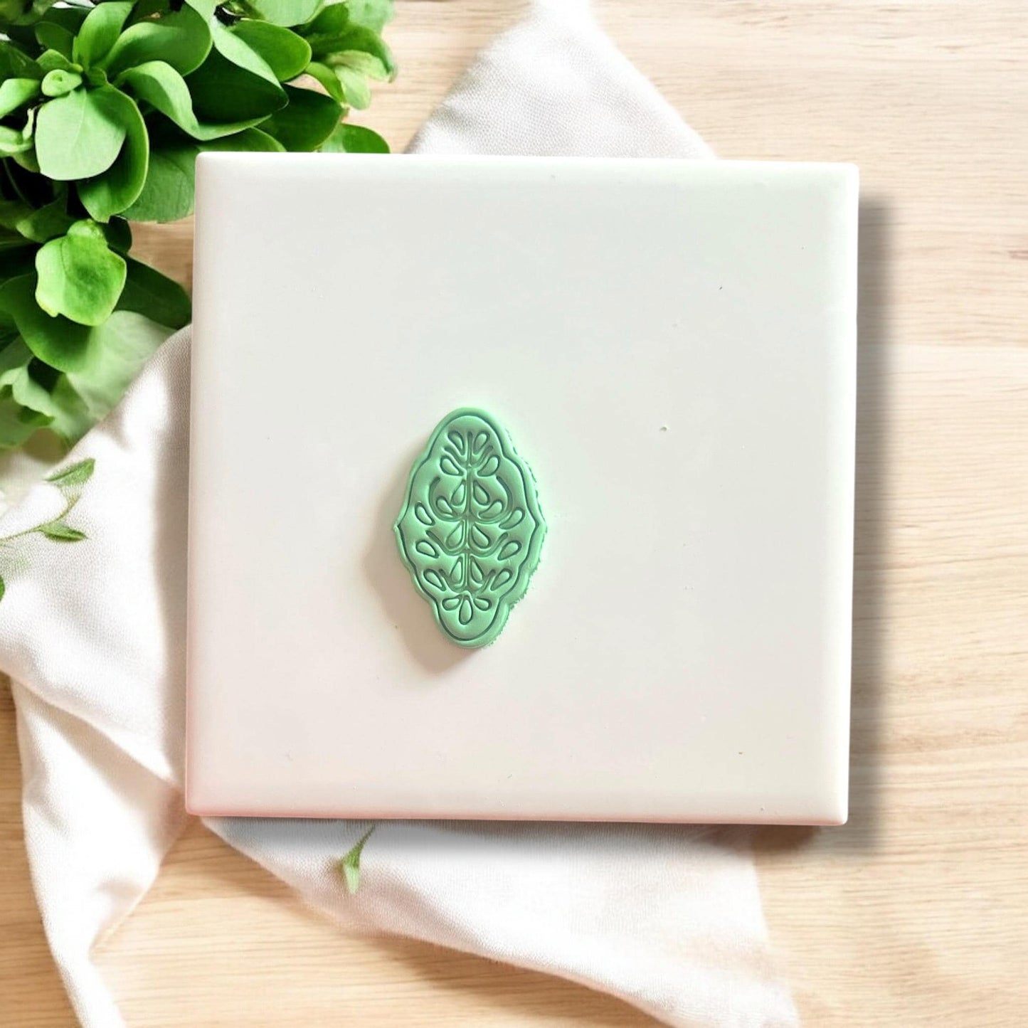 Green boho flower clay earring cutout on white tile with clean detail