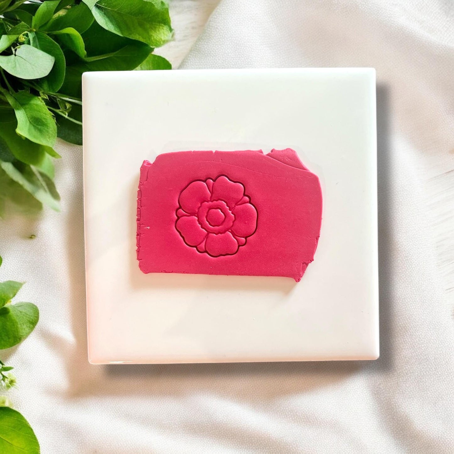 Embossed anemone flower design pressed into pink polymer clay slab on white tile