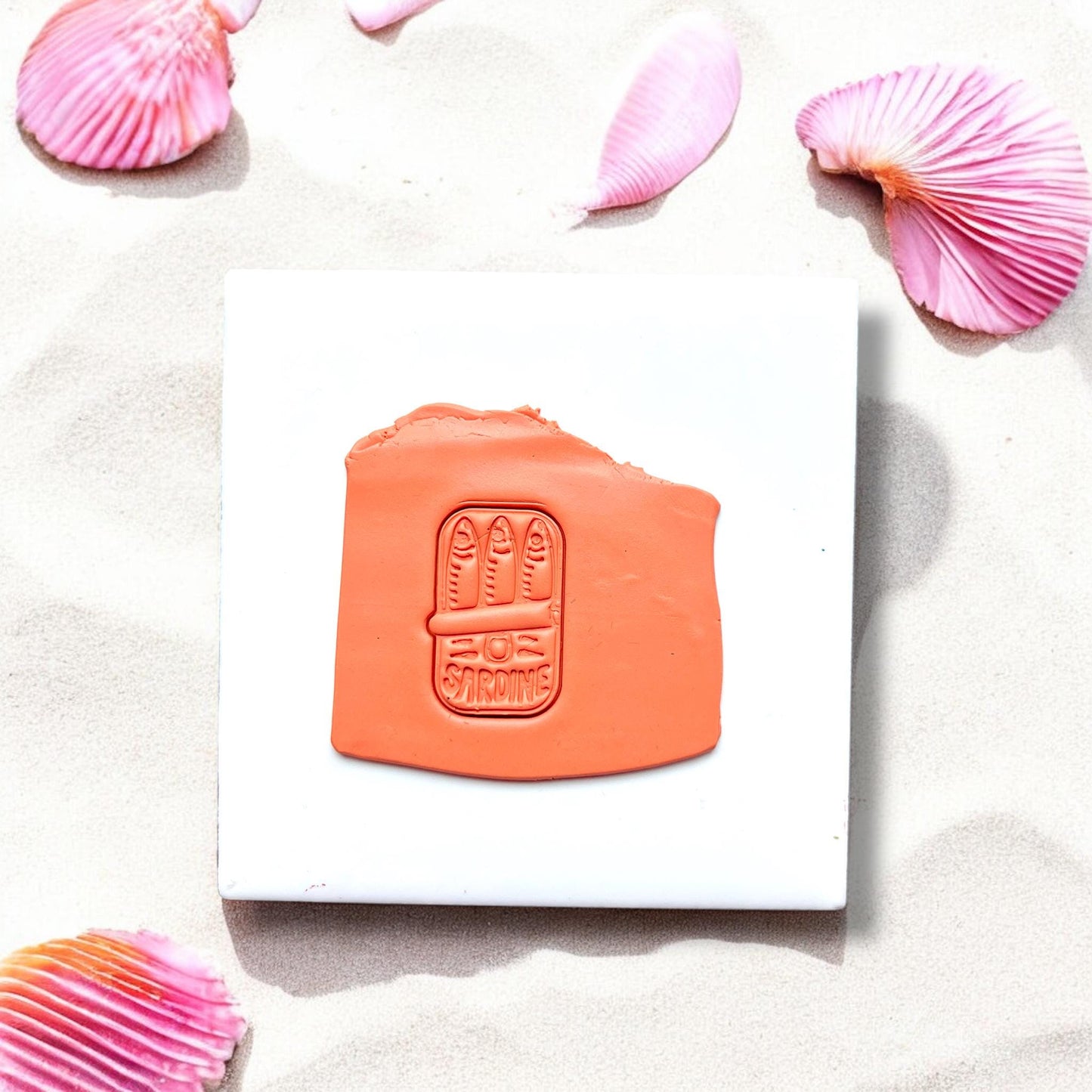 Clay impression of sardines in a can cutter on orange polymer clay