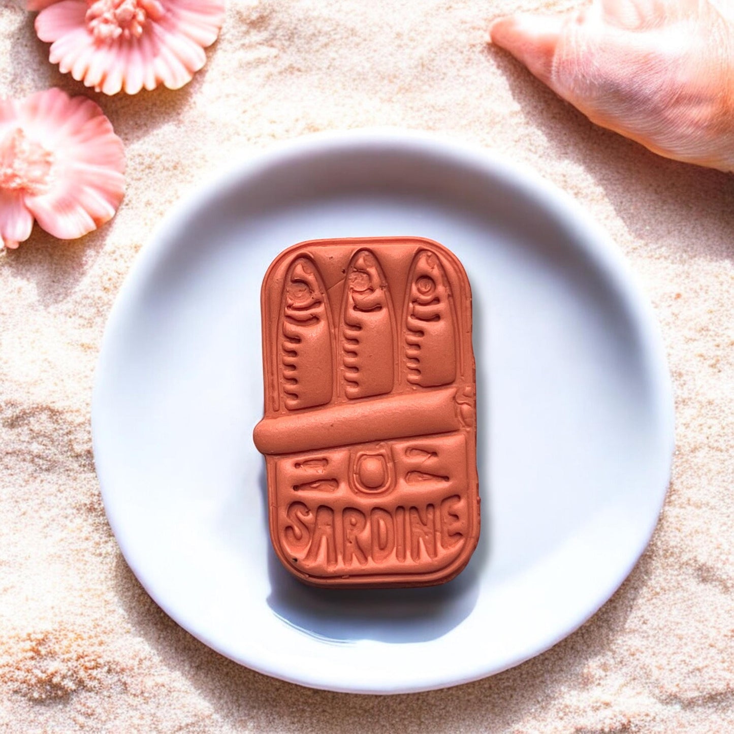 Close-up of completed sardine can clay charm on ceramic plate with beach background