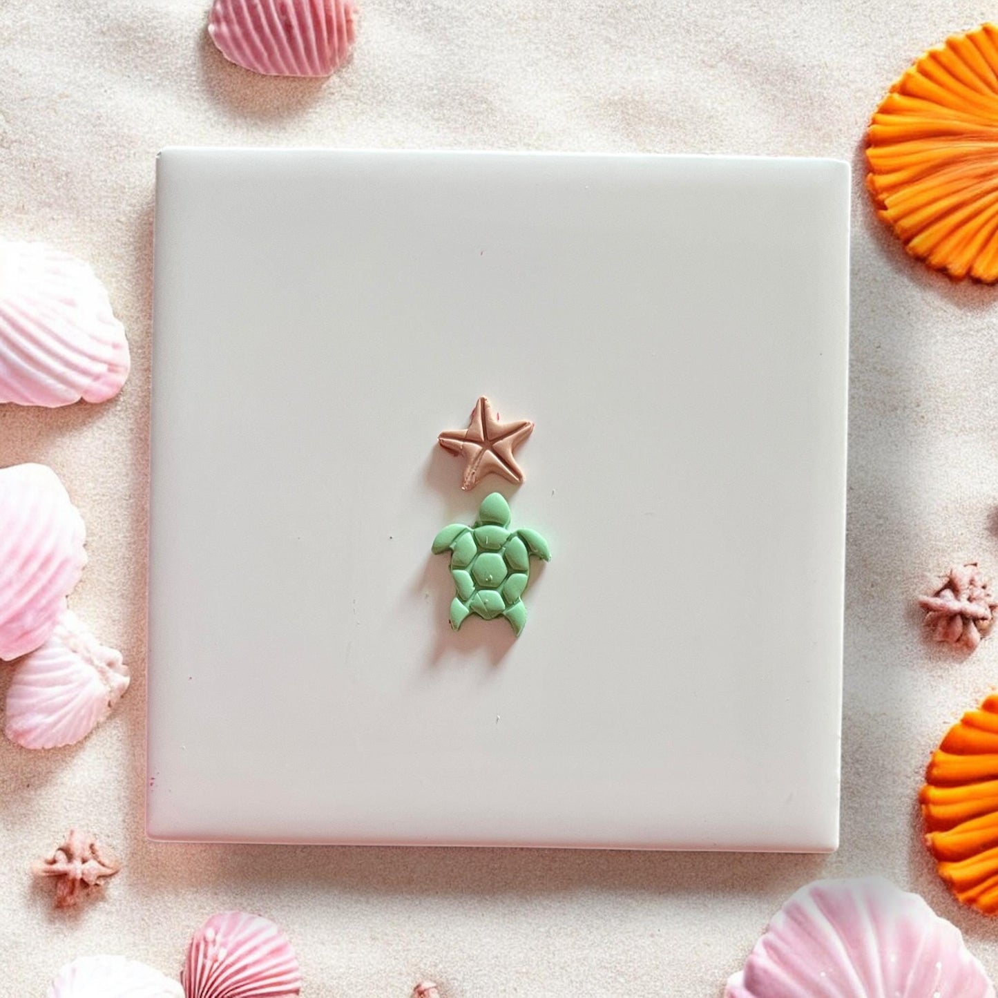 Finished green turtle and bronze starfish earring clay pieces on white tile