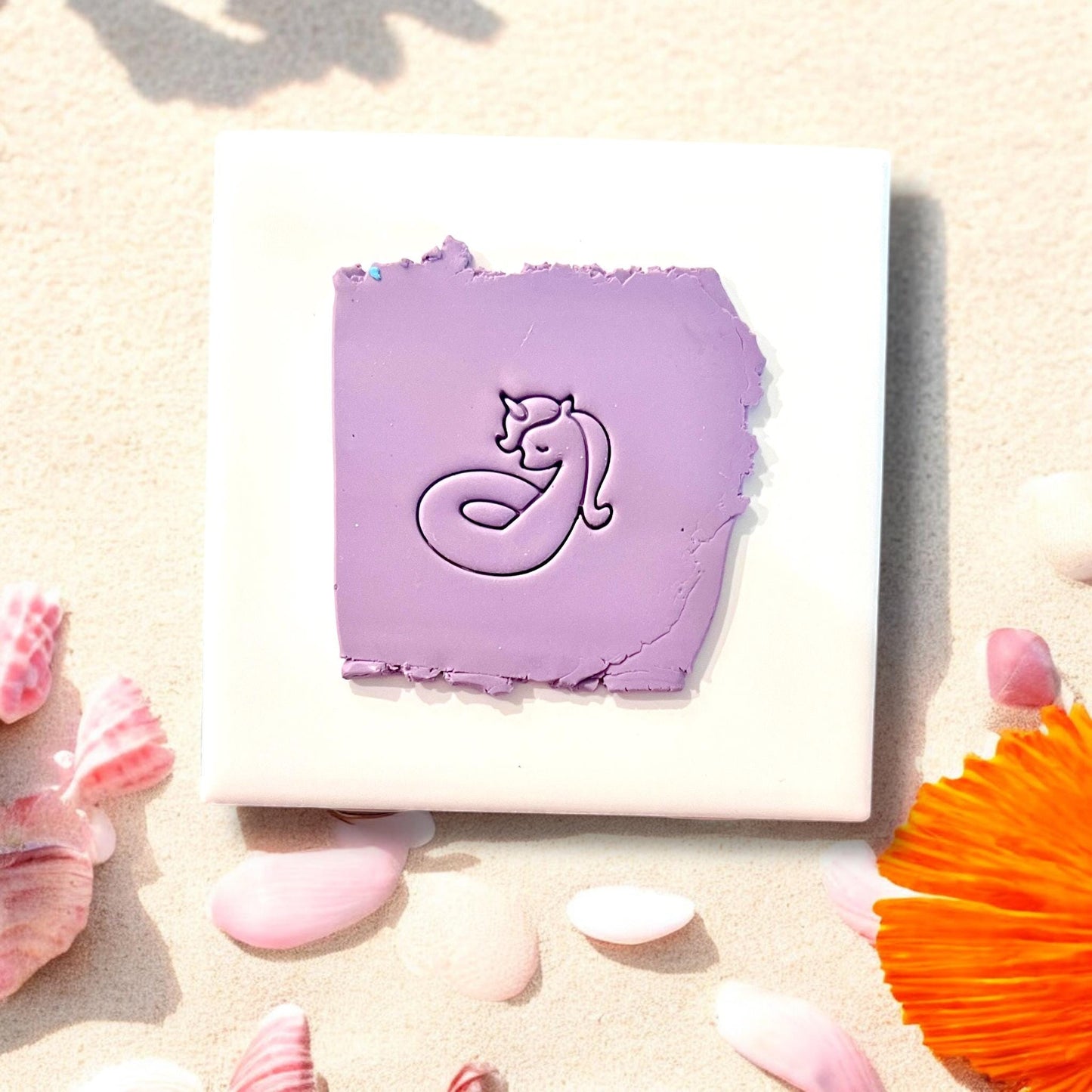 Purple unicorn floatie clay imprint on tile with beach shell accents
