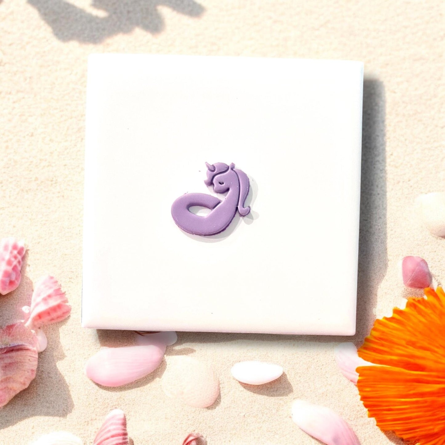 Finished purple unicorn floatie clay piece on white square tile