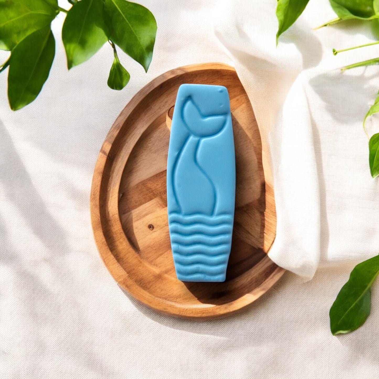 Mermaid huggie clay cutter displayed with soft green leaves and sunlight