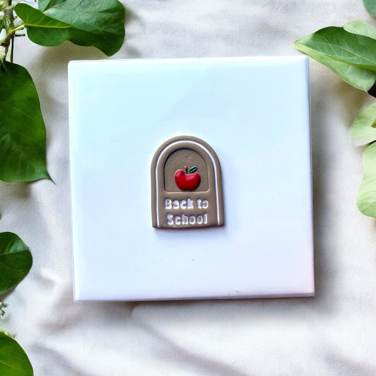 Finished clay earring with painted apple and white text