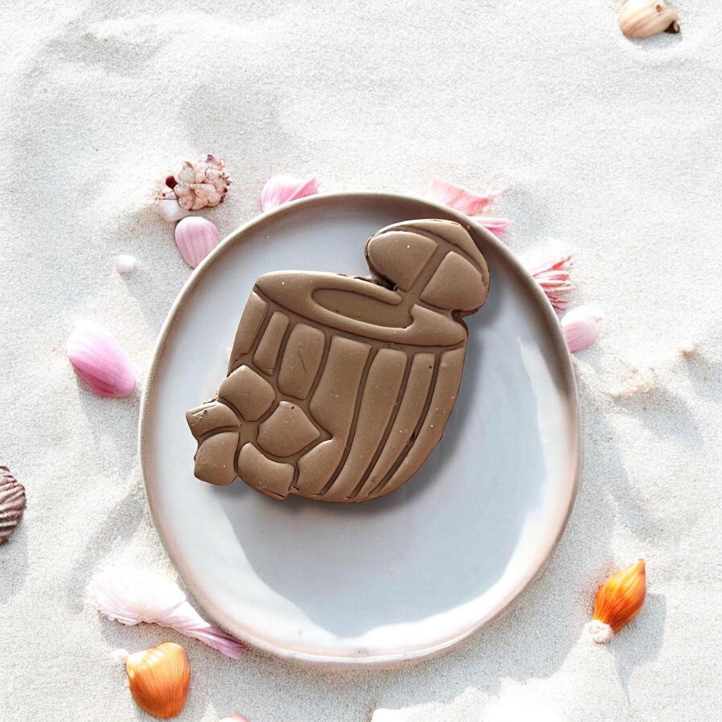 Enlarged coconut drink clay piece on plate with sand and shells