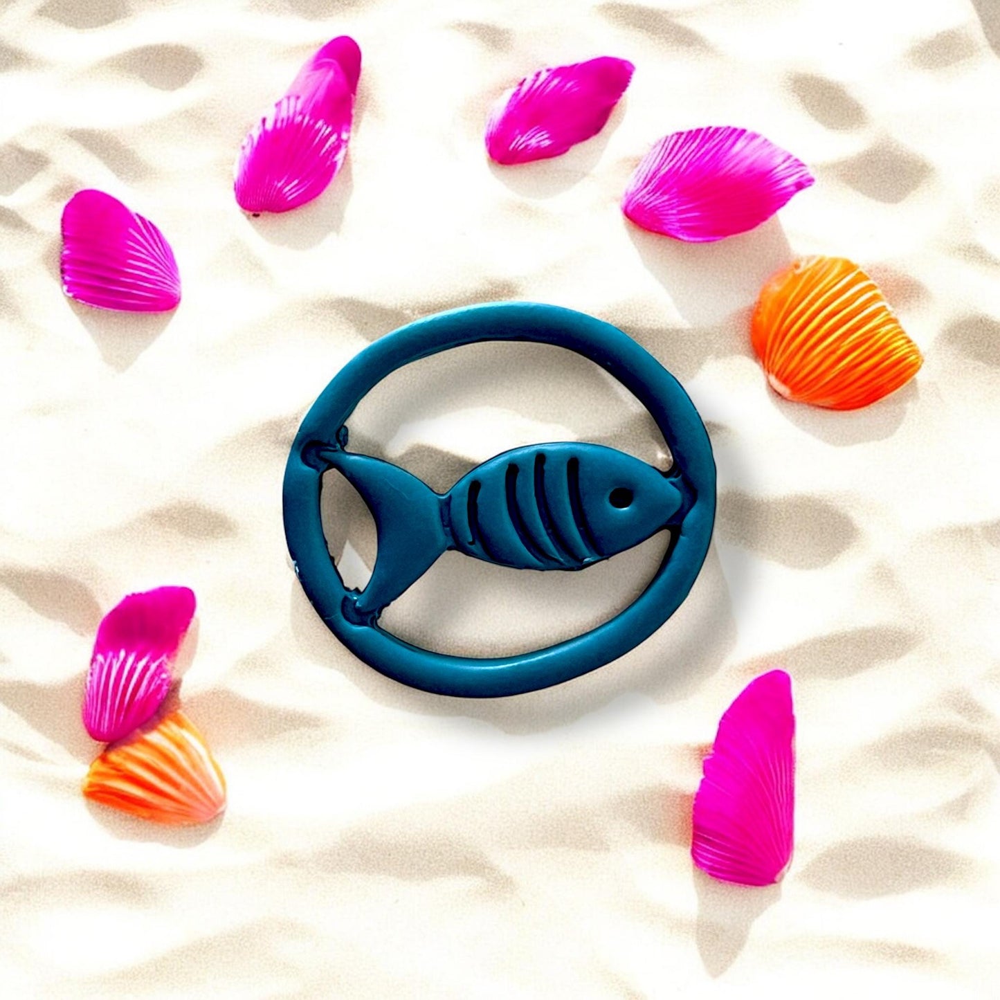 Large fish design in blue clay on beach with bright shells