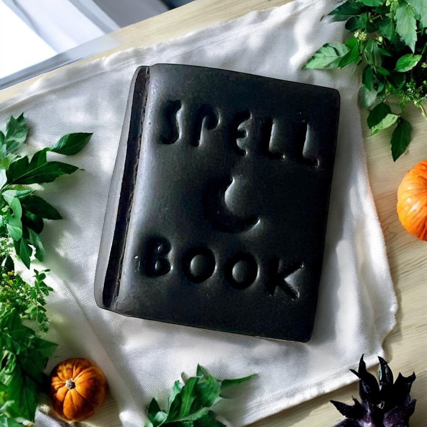 Close-up of black spell book polymer clay earring on fabric with pumpkins and greenery