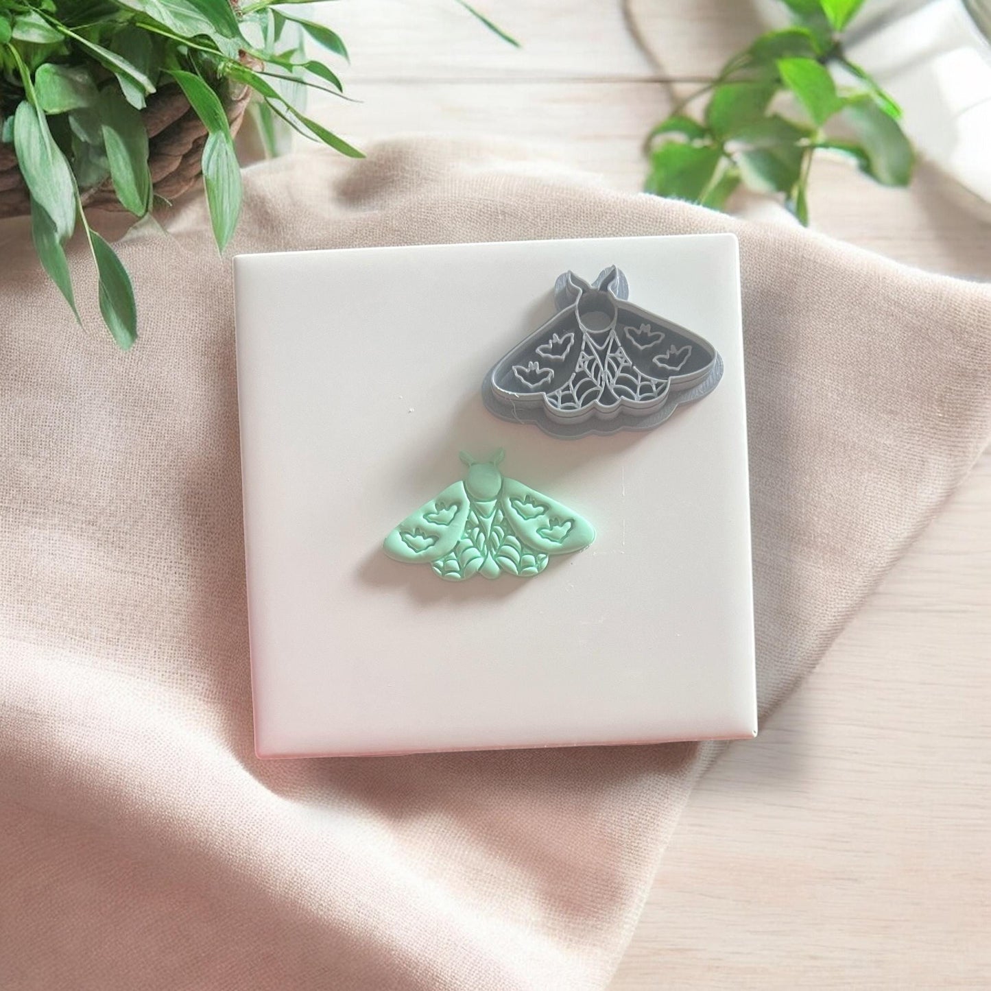Finished moth clay cutout shown next to the matching gray cutter on a soft fabric background.