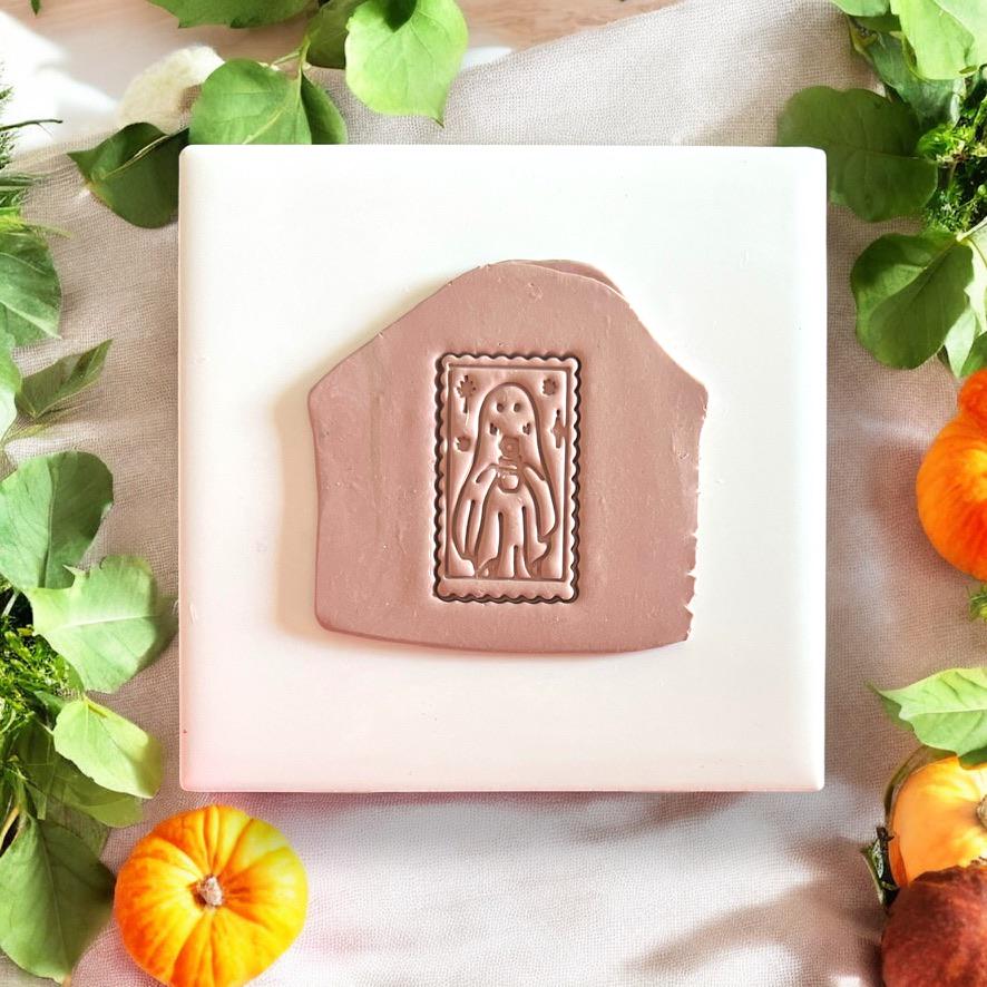 Clay slab impression of ghost cameo holding a flower with fall leaves and pumpkins