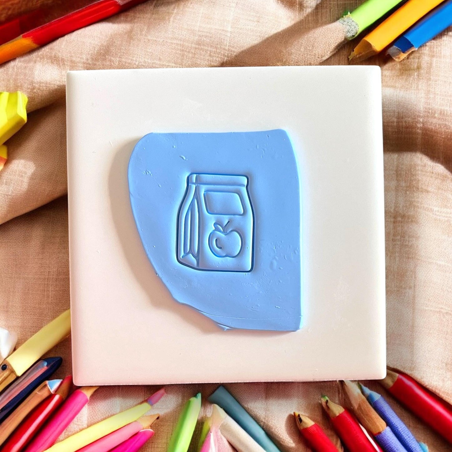 blue clay impression of a lunch bag and apple design