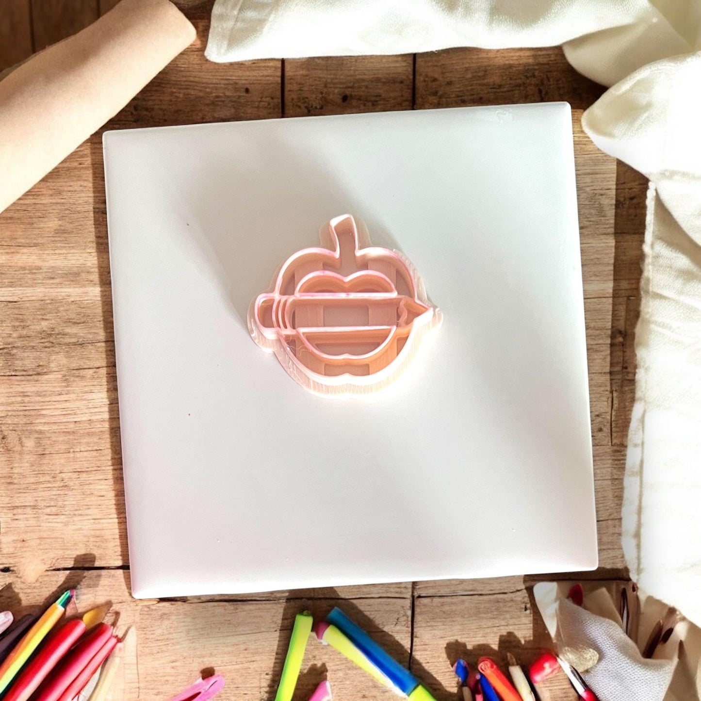 Apple and pencil cutter shown top-down on white tile