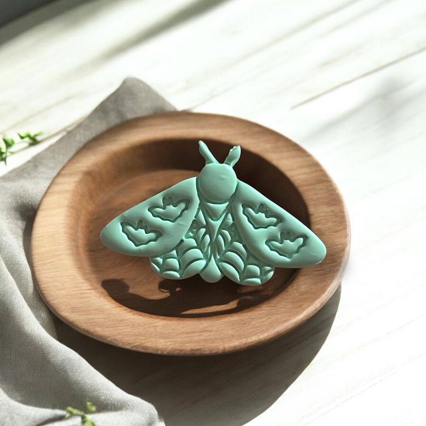 Large mint green moth clay piece with bat-shaped wing patterns shown in a wooden dish.