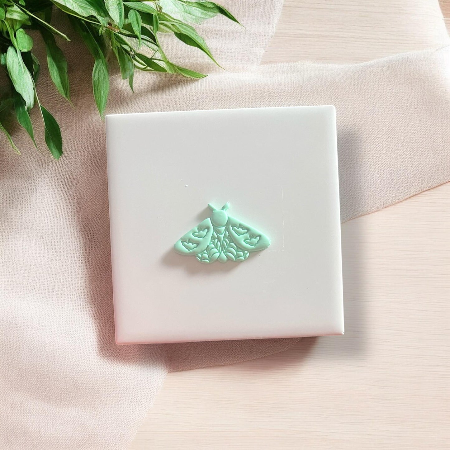 Small mint green moth cutout with bat wing detail displayed on white tile.