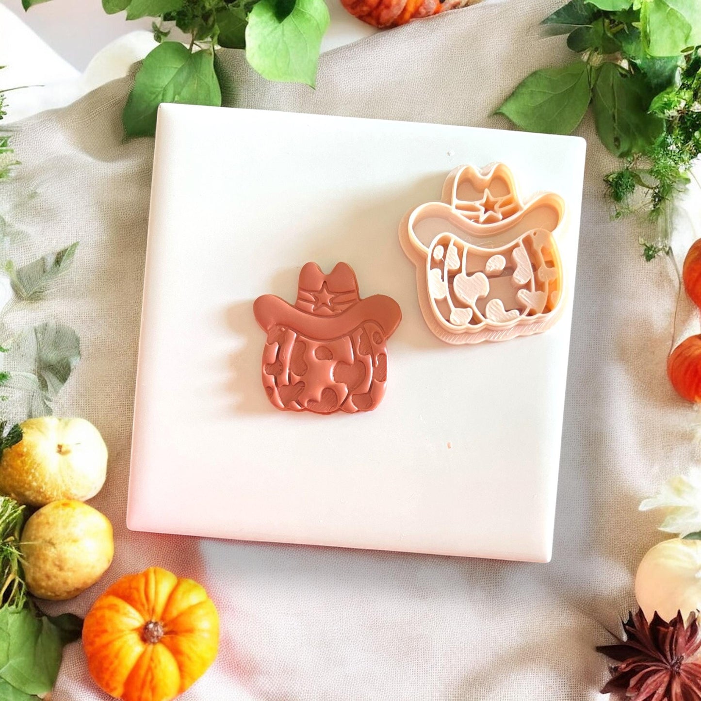 Polymer clay cutter in cowprint pumpkin shape with hat, placed on white tile