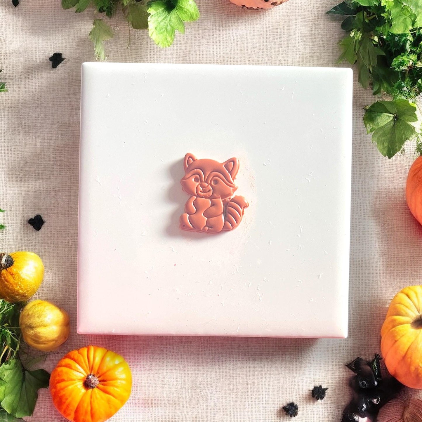 Finished clay raccoon earring with carved details shown on white tile