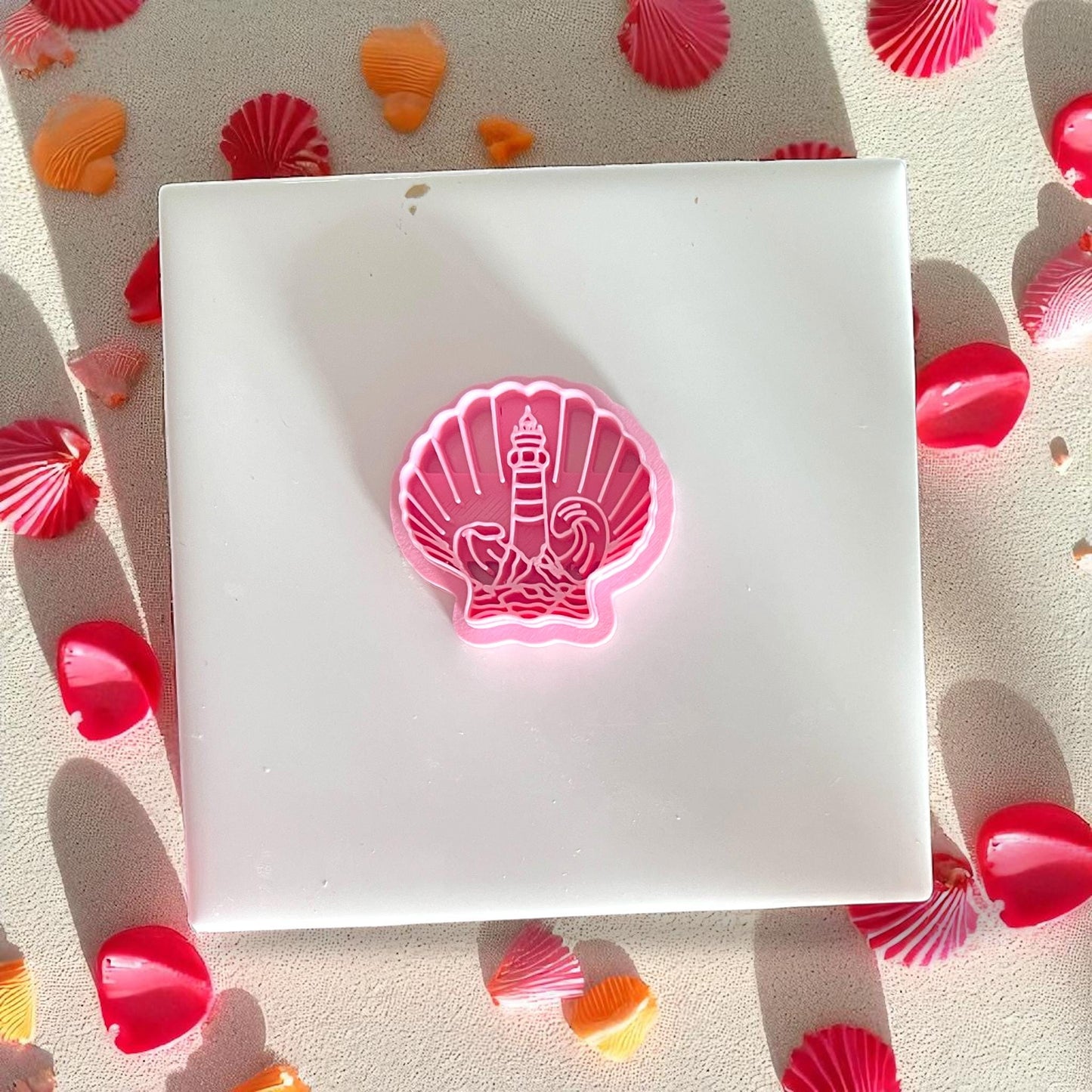 Close-up of pink lighthouse shell cutter on white tile, surrounded by beach petals